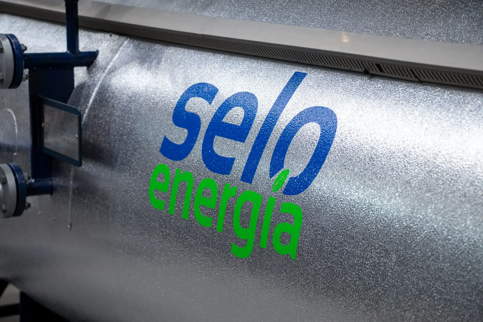 Srebrny, cylindryczny zbiornik przemysłowy z charakterystycznym, niebiesko-zielonym logo „Selo energia”.